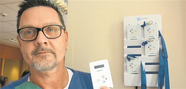 A man is holding an RTLS tag in his hand, with a wall-mounted charging station containing additional tags in the background.